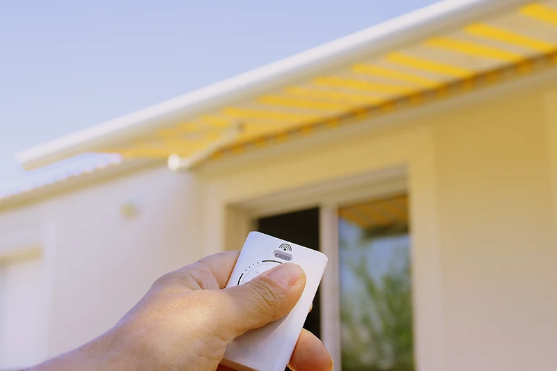 Eine Hand bedient eine motorisierte Markise mit einer Fernbedienung